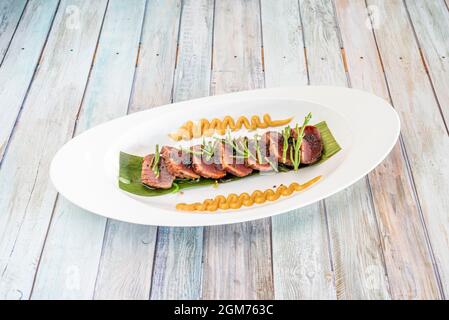 Rote Thunfisch-Tataki mit Gemüse und Samen garnieren auf einem Bananenblatt mit einer Kerosauce auf einem weißen Tablett Stockfoto