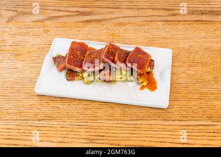 Rotes Thunfisch-Tataki mit süßer und saurer Sauce und marinierter Avocado auf weißem Teller und Holztisch Stockfoto