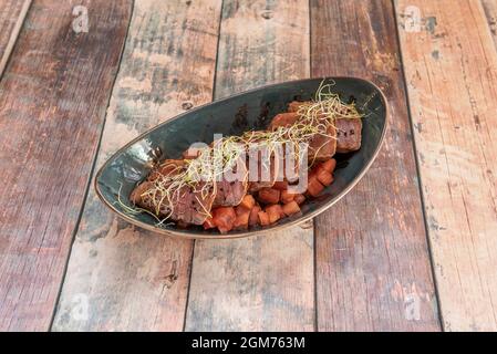 Asiatisches Rezept für rote Thunfisch-Tataki mit gewürfelten Tomaten und Bohnensprossen in einer dunklen Schüssel auf einem Holztisch Stockfoto