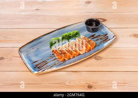 Spektakuläre Lachs-Tataki, mariniert mit Sojasauce und Sesam und Mohn, garniert mit Wakame-Salat auf einem Holztisch Stockfoto