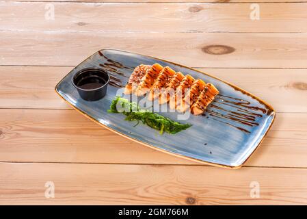 Lachs-Tataki-Rezept mit Sojasauce und Wakame-Algensalat auf blauem Teller und Holztisch garnieren Stockfoto