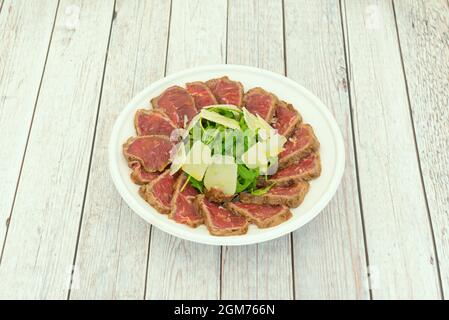 Rindfleisch-Tataki mit Parmesan-Käseflocken und ein wenig Rucola mit Öl und Salz auf einem Teller für die Hauszustellung Stockfoto