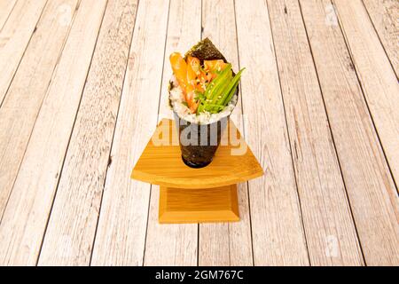 Norwegisches Lachs-Temaki-Sushi mit reifer Avocado, Sesam, Nori-Algen-Kegel auf Holzständer Stockfoto