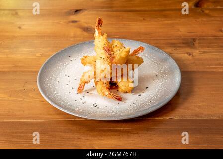 Garnelen-Tempura auf einem grauen Teller mit Sesam und Mohn auf einem Holztisch Stockfoto