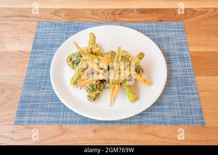 Zartes Gemüse-Tempura auf weißem Teller und blauem Untersetzer Stockfoto