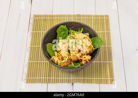 EBI-Garnelen-Tempura mit Spinat, Orangen- und Petersilienblättern, einer Sauce aus dem Laub und Bambusstamelie auf einem weißen Tisch. Stockfoto