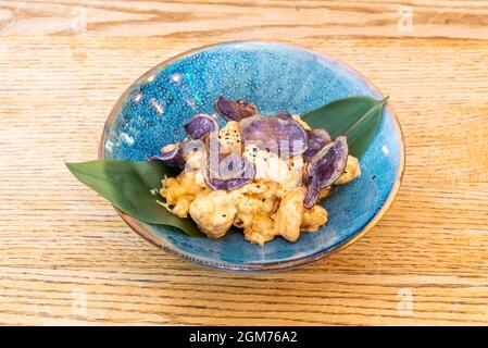 Garnelen-Tempura mit lila Kartoffelchips auf dekorativem Bananenblatt und blauer Schale auf Eichentisch Stockfoto