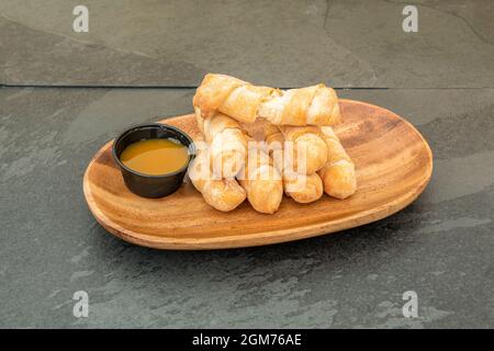 Holztablett mit tequeños zum Frühstück, eines davon oben auf einem schwarzen Schiefertisch in zwei Hälften geteilt Stockfoto