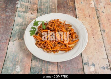 Chinesisches Rezept für würzige Rinderstreifen mit Karottenstreifen mit frischer Petersilie auf weißem Teller braten Stockfoto