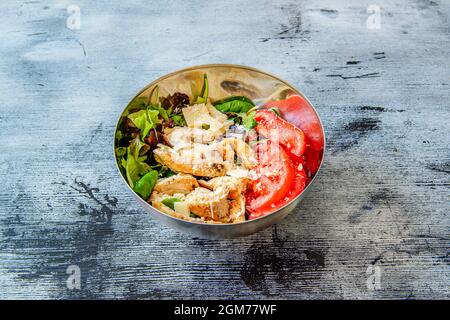 Metallschüssel mit gebratenem Huhn, Parmesan-Käseflocken, speziell geschnittenen Tomaten, Salatsprossen und weißem Reis auf der Basis auf einer blauen und bla Stockfoto