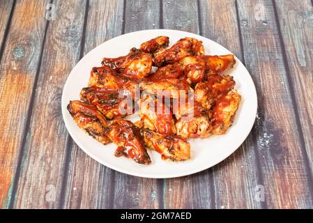 Großzügige Portion gebratener Hähnchenflügel mit Barbecue-Sauce auf Holztisch Stockfoto