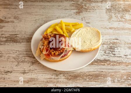 Spanisches Rezept für Hamburger mit Rindfleisch, bedeckt mit serrano-Schinken mit Scheiben von geräuchertem Käse, knuspriger Zwiebel und einer Portion Kartoffeln Stockfoto