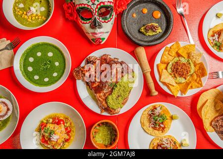 Draufsicht Foto eines roten Tisches in einem mexikanischen Restaurant mit Carnitas, Tacos al Pastor, roten Heuschrecken, Nachos mit Guacamole und viel Farbe und ein Stockfoto