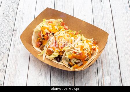 Papptablett mit drei Tacos mit Weizentortillas, mit Kürbiscreme, schwarzen Bohnen, Cheddar-Käsesahne und geriebenem Käse Stockfoto