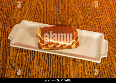 Köstliches Tiramisu-Dessert mit Kakaopulver und Vanille auf einem rötlichen Holztisch. Stockfoto