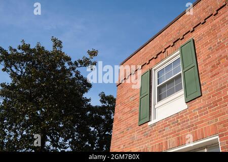 Ein Eckfenster mit holzgrünen Fensterläden eines alten roten Backsteingartenapartments an einem sonnigen Nachmittag. In Arlington, Virginia, in der Nähe von Washingto Stockfoto