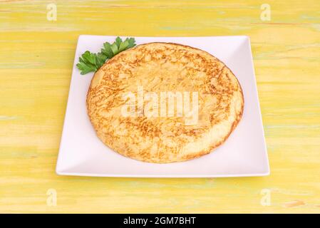 Omelette mit Kartoffeln und Eiern auf einem weißen quadratischen Teller auf einem gelben Holztisch serviert Stockfoto