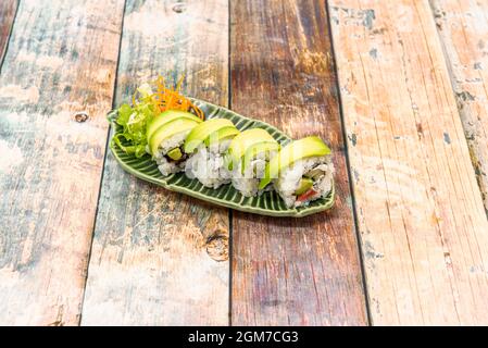 Uramaki-Rolle mit weißem Reis, gefüllt mit tropischen Früchten und Avocado-Scheiben darauf Stockfoto