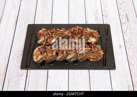 Sushi-Uramaki-Hähnchen in Tempura mit Speckstreifen und Sojasauce darauf Stockfoto