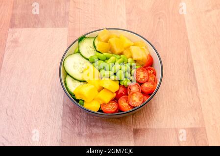 Tropische Schüssel mit Ananas, Avocado und Mango mit gehackten rohen Gurken, gehackten Kirschtomaten, edamame Bohnen mit weißem Reis als Basis. Stockfoto