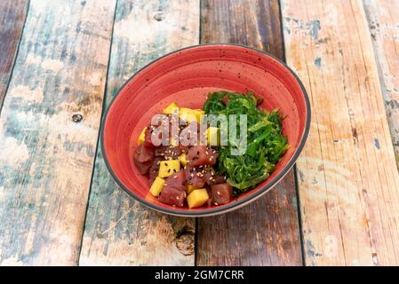 Rote Thunfisch-Tartare mit gewürfelter Mango, Mohnsamen und Sesam und Wakame-Algensalat auf einer roten Schüssel Stockfoto