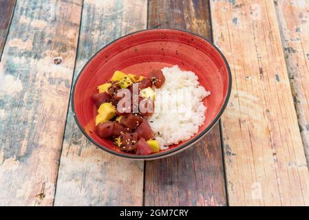 Rote Thunfisch-Tartare mit Mango, Mohnsamen und Sesamwürfeln mit weißem Reis auf einer roten Schüssel Stockfoto