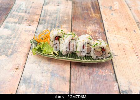 Roter Thunfisch, roter Thunfisch, Maguro in Rolle mit Pfeffer, Avocado, Reis, Schnittlauch und Sesam auf Holztisch Stockfoto