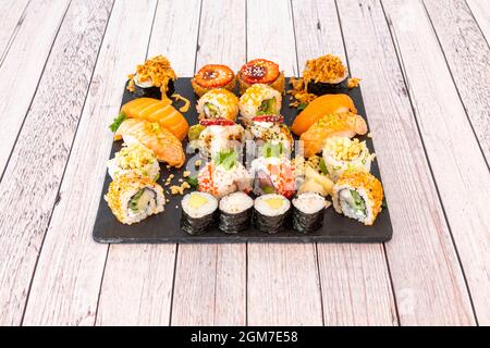 Gemischtes Sushi-Tablett mit Nori-Algen-Maki, Uramaki california Roll mit Masso-Rogen, rohem Lachs Nigiri, flambiertem Lachs, knusprigen Zwiebeln, Frischkäse und Stockfoto