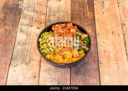 Schwarze Schale mit hawaiiianischem Poke mit norwegischem Lachs, knusprigen Zwiebeln, japanischem Edamame, afrikanischer Mango und Wakame-Algensalat. Stockfoto