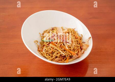 Weiße Schüssel mit sautierten Nudeln mit frischem Gemüse und Yakisoba-Sauce auf dem orangefarbenen Tisch Stockfoto