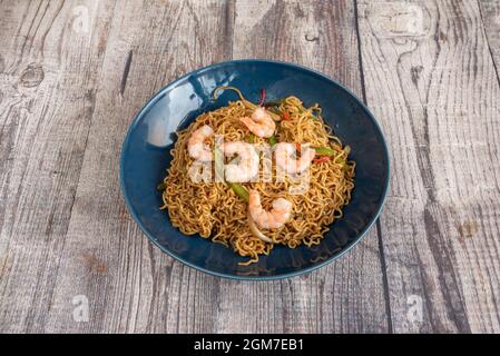 Sautierte Nudeln mit Gemüse und Garnelen mit Yakisoba-Sauce auf einem blauen Teller Stockfoto