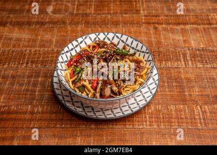 Köstliche Nudeln, die mit asiatischem Fleisch, Gemüse und Samen in Yakisoba-Sauce mariniert sind Stockfoto