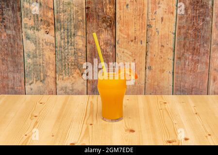 Kristallglas mit Stroh und Scheibe am Rand von frisch gepresstem Orangensaft Stockfoto