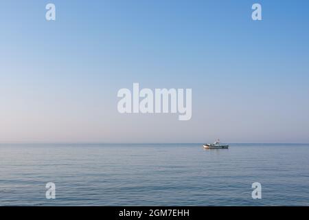 An einem ruhigen Tag bei Sonnenaufgang liegt ein kleines Motorboot vor der Küste einer türkischen Insel in der Ägäis Stockfoto