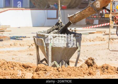 Betonmischwagen, der Flüssigbeton in den Turmkraneimer auf der Baustelle, Close Up, gießt Stockfoto