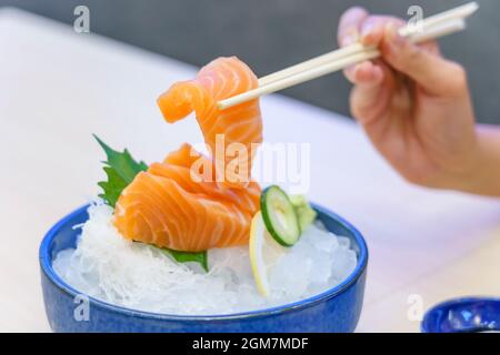 Lachs-Sashimi mit Essstäbchen in der Hand halten: Roher, frischer Lachs in Scheiben geschnitten, serviert auf Eis mit Wasabi, japanischer Küche. Stockfoto