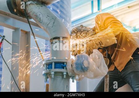 Schwerindustrie Arbeiter Schleifen Stahlrohr mit Verschleiß Schutzmaske durch elektrische Schleifscheibe auf Baustelle. Stockfoto