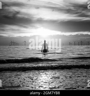 Ein quadratisches Bild einer Iron man-Statue am Crosby Beach, Teil von Antony Gormleys Installation Another Place, die im September bei Sonnenuntergang zu sehen ist Stockfoto