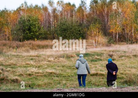 Unschärfe-Effekte von zwei Frauen bei einem Spaziergang in der herbstlichen Natur. Herbsthintergrund. Wunderschöne Landschaft. Zwei Frauen, die im Herbstwald entlang der Straße spazieren Stockfoto