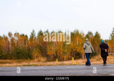 Unschärfe-Effekte von zwei Frauen auf einem Spaziergang im Herbst Natur überqueren die Straße. Zwei Frauen, die im Herbstwald entlang der Straße spazieren. Rückansicht. Aus FOC Stockfoto