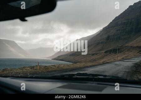 Fahren auf den Färöer Inseln. Skandinavische Natur, braune Felder und Hügel, launischer Himmel. Leere Straße Stockfoto