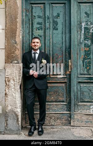 Portrait des Bräutigams, der am Hochzeitstag vor der alten grünen Holztür steht. Stockfoto