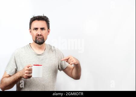 Dunkelhaariger, bärtiger Mann in grauem Hemd; mit dem Ausdruck, dass er Kaffee oder Tee möchte, mit einer Hand, die eine Tasse hält. Konzept aufwachen. Speicherplatz kopieren und whit Stockfoto