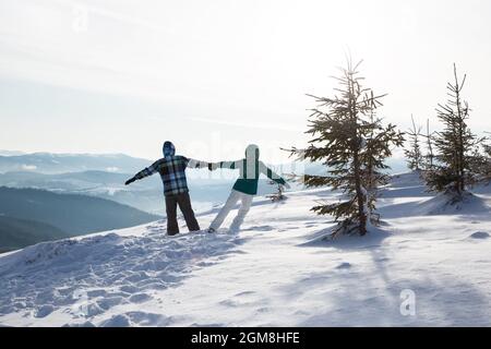 Unverkennbares verliebtes Paar in warmer Kleidung vor dem Hintergrund der malerischen verschneiten Landschaft in den Bergen steht mit Händen. Reise nach Mountain RE Stockfoto