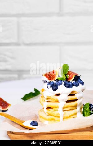 Pfannkuchen mit Heidelbeere, Feigen, Joghurt und Minze auf weißem Hintergrund, traditionelles amerikanisches gesundes Frühstück, Copyspace, vertikale Auflösung Stockfoto
