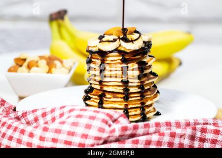 Pfannkuchen mit Schokoladensirup, Nüssen und Bananen. Stapel mit dem ganzen Flapjack. Schokolade wird in Slapjack gegossen, leckeres Frühstück und gesundes Essen Stockfoto