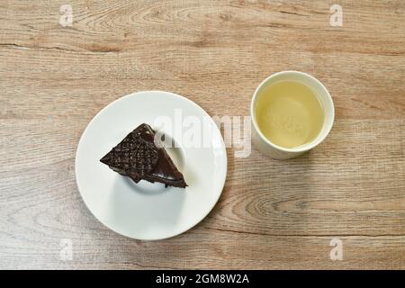 Schwarzer Waldkuchen mit Sahneteller und heißer Teetasse auf dem Tisch Stockfoto