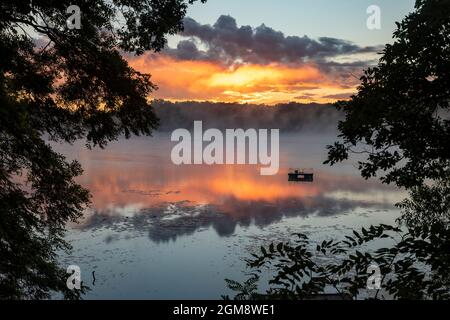 Prairieville, Michigan - Ein Schwimmfloß schwimmt auf dem ruhigen Wasser, während die Sonne über dem Stewart Lake im Westen von Michigan aufgeht. Stockfoto