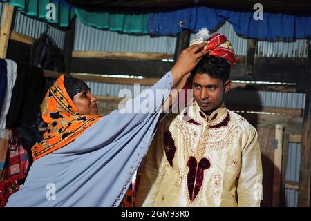 Mongla, Bangladesch. September 2021. Ein Verwandter hilft, einen Hochzeitsturban auf dem Kopf des 18-jährigen Bräutigams anzupassen, Ibrahim an seinem Hochzeitstag in einem Dorf namens Joymoni aus einem Küstengebiet von Mongla im Bezirk Bagerhat.Bangladesch erlebte während der Pandemie Covid-19 im vergangenen Jahr einen Anstieg der Kinderehen um 13 %, da das tödliche Virus die Gesellschaften und Volkswirtschaften massiv beeinflusste und viele in extreme Armut drängte. Die Abteilung für Geschlechtergerechtigkeit und Diversität von Brac, der weltweit größten NGO, fand heraus, dass die Kinderehe um 13 % gestiegen ist, als sie eine Umfrage durchführte, um auf die Auswirkungen der zuzugreifen Stockfoto