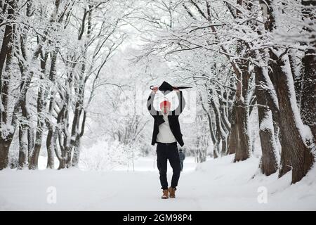 Ein Mann auf einem Spaziergang im Park. Junger Mann mit Regenschirm unter dem Winterschnee. Stockfoto